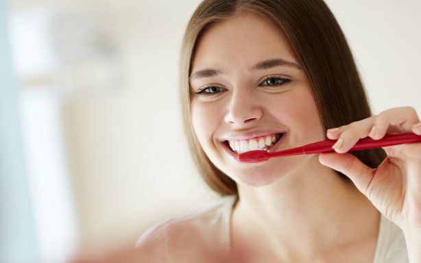 Woman smiling as she brushes her teeth in the mirror